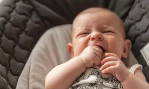 Un bebé de 3 meses no duerme, con los ojos cerrados y la mano en la boca, en una hamaca acolchada.