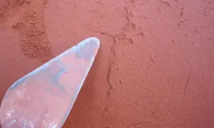 Una espátula rosa aplica mortero rojizo a una pared texturizada.