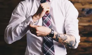 Mężczyzna w białej koszuli i krawacie poprawia mankiet, odsłaniając tatuaż na ramieniu. Czy prawnik może mieć tatuaż? Tak!