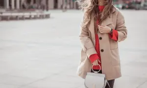 Kobieta w beżowym płaszczu i jaskrawym, czerwonym swetrze damskim. Stylizacje na chłodne dni.
