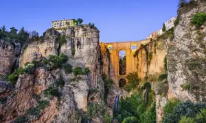 El Puente Nuevo de la Ronda, Málaga, se alza majestuoso sobre un profundo tajo, con cascadas y vegetación adornando sus acantilados.