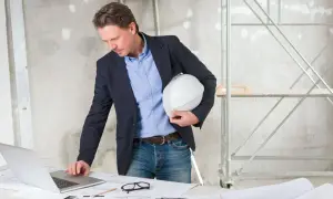 Inspektor nadzoru inwestorskiego analizuje plany na laptopie, trzymając biały kask.