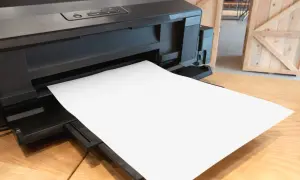 Czarna drukarka z pustą kartką papieru wysuniętą z podajnika.