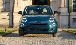 Nowy Fiat 500 w kolorze głębokiej zieleni, z charakterystycznymi okrągłymi światłami, zaparkowany przed zabytkowym budynkiem. Sprawdź aktualną fiat 500 cena!