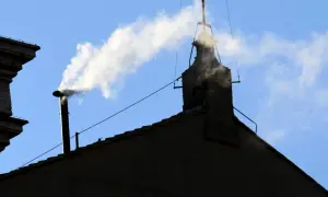 Biały dym z komina, jak sygnał wyboru nowego papieża, unosi się na tle błękitnego nieba.