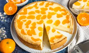 Ein saftiger faule weiber kuchen mit Mandarinenstücken, der auf einem Teller liegt. Daneben liegen frische Mandarinen und eine Tortenschaufel.
