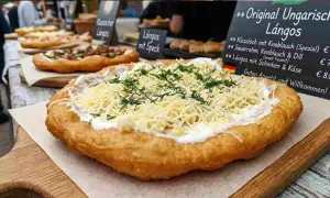 Frisch frittierter Lángos-Teig, belegt mit Sauerrahm, geriebenem Käse und Dill. Daneben weitere Lángos-Varianten.
