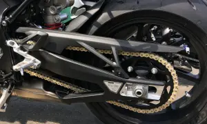 Detaljbild på en motorcykels bakparti med ett gyllene kedjespel mc som löper över ett svart drev. Däcket är ett Michelin.