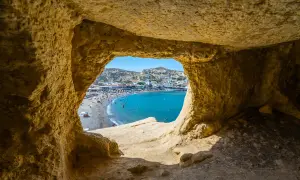 Blick durch eine Höhle auf einen belebten Strand und das türkisfarbene Meer. Ein perfekter Ausschnitt der Kreta Highlights.