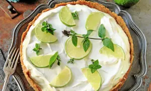 En krämig key lime pie med limeklyftor och mynta på en krispig botten.