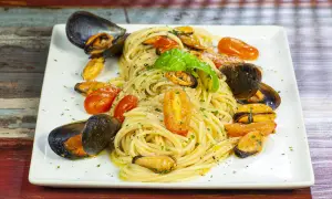 Un invitante piatto di spaghetti con le cozze e pomodorini, guarnito con basilico fresco.