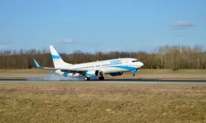 Samolot Enter Air ląduje, koła dotykają pasa, unosząc pył.