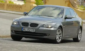Szary sedan BMW E60 z włączonymi światłami. Widać charakterystyczne żarówki BMW E60, które oświetlają drogę.