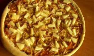 Pyszna pizza z ananasem i szynką, zrumieniona skórka i złocisty ser.
