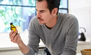 Uomo pensieroso guarda una fiala di liquido giallo, chiedendosi se la vitamina B12 fa ingrassare.