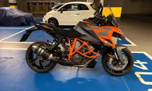 Pomarańczowo-szary KTM 1290 Super Duke w garażu, obok białego Fiata 500.