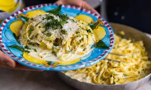 En tallrik med krämig pasta al limone, toppad med parmesan och persilja, serveras från en panna.