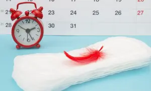 Brązowe plamienie po okresie, symbolizujące delikatne sygnały ciała, obok podpasek i budzika odmierzającego czas.
