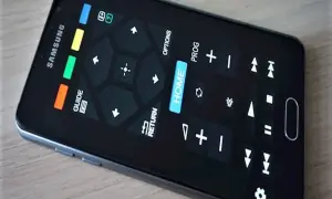 Smartfon z ekranem imitującym aplikację pilot do telewizora. Widoczne przyciski nawigacyjne, "HOME", "GUIDE", "RETURN" i inne funkcje.