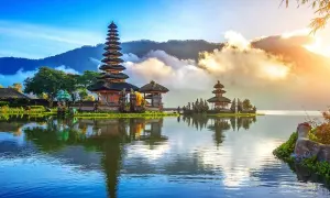 Świątynia Pura Ulun Danu Bratan na Bali, odbijająca się w spokojnej tafli jeziora, otoczona górami i chmurami.