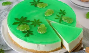 Grüne Philadelphia Torte Waldmeister mit Gummifröschen und Blättern verziert. Ein Stück wird gerade herausgeschnitten.