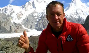 Bergsteiger Denis Urubko gibt Daumen hoch vor schneebedeckten Gipfeln.