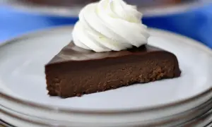 En bit krämig fransk chokladtårta med en virvel av vispgrädde på en tallrik.