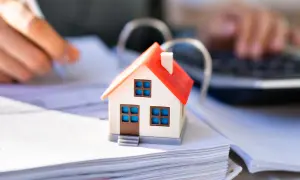 Hausmodell auf Dokumenten, Hände schreiben und tippen. Berechnung der Hessen Grunderwerbsteuer für den Hauskauf.