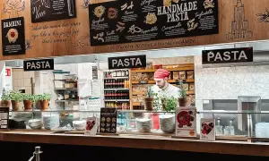 W Vapiano kucharz przygotowuje ręcznie robiony makaron. Na ścianie menu z różnymi rodzajami pasty.