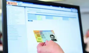 Mano sostiene DNI español frente a pantalla de ordenador con interfaz de gestión. Apoderamiento DGT.