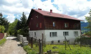 Stacja turystyczna Abrahamów, drewniano-betonowy budynek z czerwoną dachem, otoczony zielenią i polnymi kwiatami.