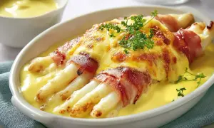 Spargel in Schinken eingerollt, überbacken mit Käse und serviert in einer cremigen Sauce.