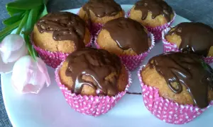 Pyszne muffiny z powidłami śliwkowymi, polane czekoladą, na talerzu z tulipanami.
