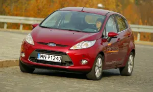 Czerwony Ford Fiesta 2009 z kierowcą za kierownicą, jadący po drodze.