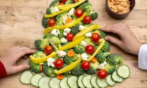 Une joyeuse planche apéritif noël en forme de sapin, décorée de brocolis, tomates cerises, poivrons jaunes, chou-fleur et rondelles de concombre.