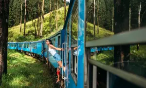 Pociąg Sri Lanka mknie przez zielone wzgórza. Kobieta wychyla się z okna, ciesząc się widokiem.