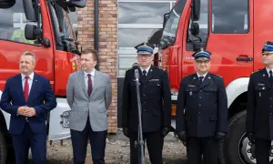Uroczystość przed remizą OSP. W garniturach i mundurach strażackich stoją mężczyźni, wśród nich zastępca naczelnika OSP.
