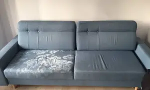 Szara kanapa z plamami na jednym siedzisku. Pokazuje, jak wyczyścić tapicerkę, by odzyskać jej pierwotny wygląd.