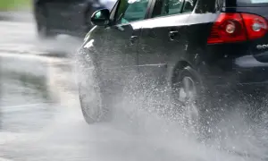 Un coche negro salpica agua al pasar por un charco. En días de lluvia, una distancia de frenado segura depende de la precaución.