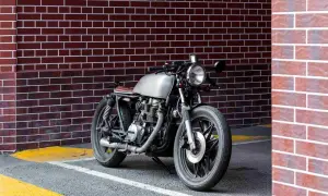 Stylowy motocykl miejski z metalicznym bakiem i brązowym siedzeniem stoi przy ceglanej ścianie.