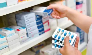 Ręka farmaceuty wybiera z półki lek, w tym antybiotyk azytromycyna w blistrach.
