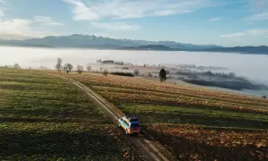 Samochód przemierza malownicze **Ponidzie**, gdzie mgła otula doliny, a w oddali rysują się ośnieżone góry.