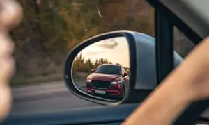 Reflejo de un coche rojo en el espejo retrovisor, preparándose para un adelantamiento. DGT.