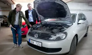 Två män inspekterar motorutrymmet på en silverfärgad kombi. En av dem pekar mot motorn, kanske för att diskutera kamremmen på 1.4 TSI-motorn.