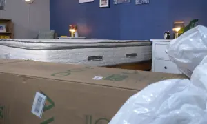 A mattress that expands when opened is shown, partially covered by a cardboard box and plastic packaging.
