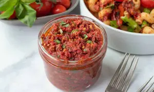 Vaso di pesto di pomodori secchi pugliese, pronto per condire la pasta. Freschi pomodori e basilico sullo sfondo.