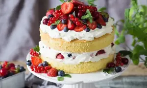 Puszysty tort z bitą śmietaną i mascarpone, ozdobiony świeżymi truskawkami, borówkami i porzeczkami. Idealny na letnie przyjęcie.