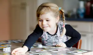 Niña rubia con coletas jugando a un juego de memoria infantil, concentrada en las cartas sobre la mesa.