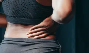 Kobieta trzymająca się za bolący bok, w czarnym sportowym topie i spodenkach.