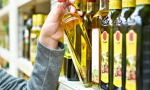 Ręka wybiera butelkę oliwy z oliwek. Czy oliwa z oliwek może zamarznąć? Niska temperatura może spowodować jej zmętnienie, ale nie zepsuje jej.